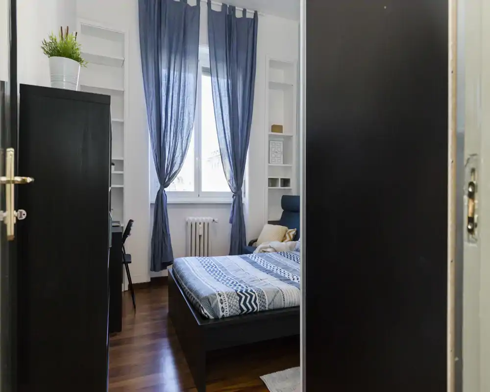 Camera da letto luminosa e arredata con letto matrimoniale, biancheria a motivi e tende blu che incorniciano una finestra luminosa — accogliente e pronta per gli ospiti.