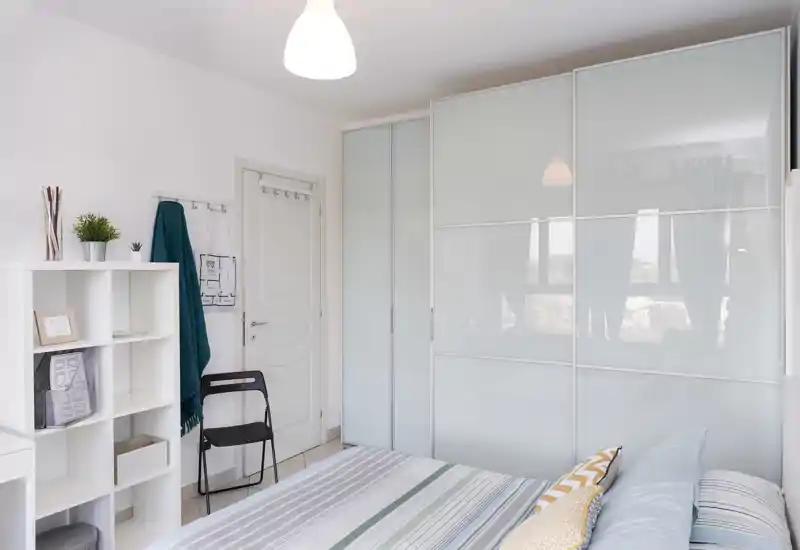 Bright, modern bedroom with a striped bed, decorative pillows and large frosted sliding wardrobe; clean minimalist styling and natural light.