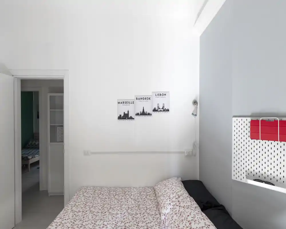 Dormitorio luminoso y minimalista con una cama doble de estampado, paredes blancas y láminas con siluetas de ciudades. Estilo moderno y luz natural suave, perfecto para fotos de alquiler.