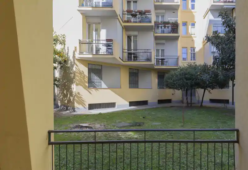 Vista su un cortile condominiale con prato visto da un balcone coperto, con gli altri balconi dell'appartamento e fioriere che si affacciano sullo spazio.