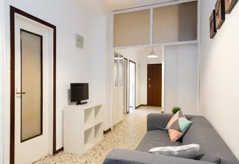 Soggiorno compatto e ben illuminato con un divano grigio comodo, cuscini decorativi e un piccolo mobile TV — ideale per un appartamento in città.