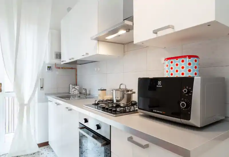 Cucina moderna e luminosa con piano cottura a gas, forno integrato, lavello e microonde su un piano di lavoro pulito — ideale per soggiorni brevi.