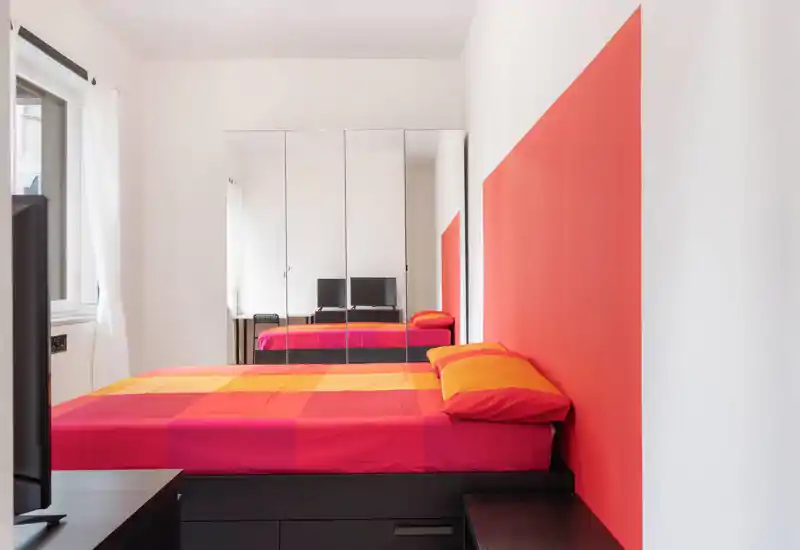 Camera da letto luminosa e moderna con letto matrimoniale colorato, armadio con ante a specchio e luce naturale dalla finestra — elegante e pronta per gli ospiti.