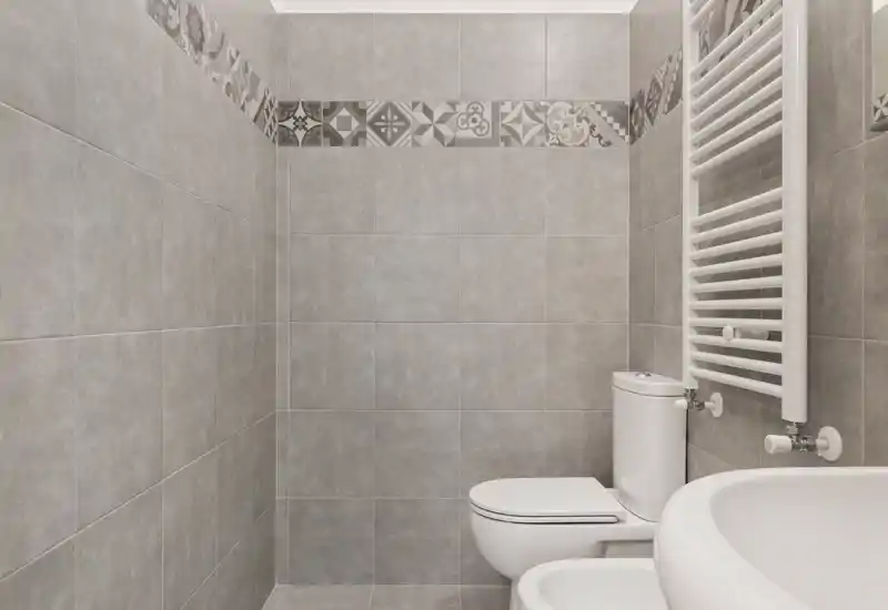 Bagno moderno e pulito con pareti rivestite in piastrelle grigie, WC, bidet e scalda-salviette bianco; toni neutri e finiture contemporanee.