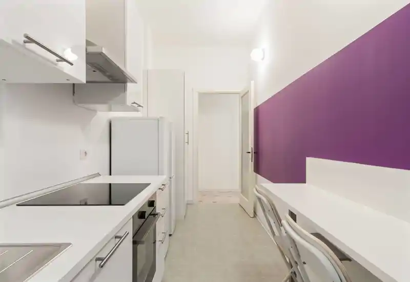 Cucina moderna a corridoio, luminosa, con mobili bianchi, piano cottura a induzione e un compatto piano di lavoro/pranzo lungo la parete — ideale per uno studio o piccolo appartamento.