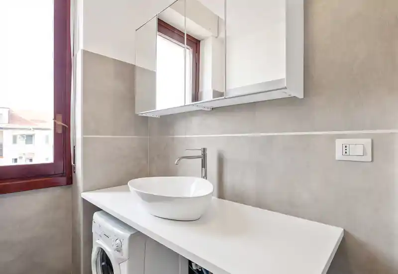 Bright, modern bathroom corner with a vessel sink, wall-mounted mirror cabinet and a window providing natural light.