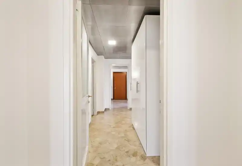 Bright, clean entrance corridor with built-in white storage cabinets and polished stone floor leading to the main door; neutral walls and overhead lighting create a welcoming first impression.
