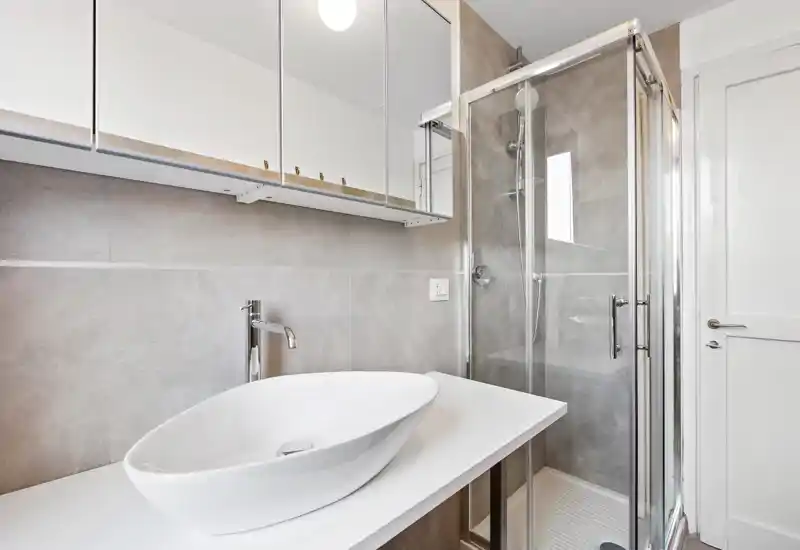 Modern, bright bathroom with a freestanding basin, large mirror cabinets and a glass shower enclosure. Clean lines and neutral tiles create a contemporary, elegant feel.