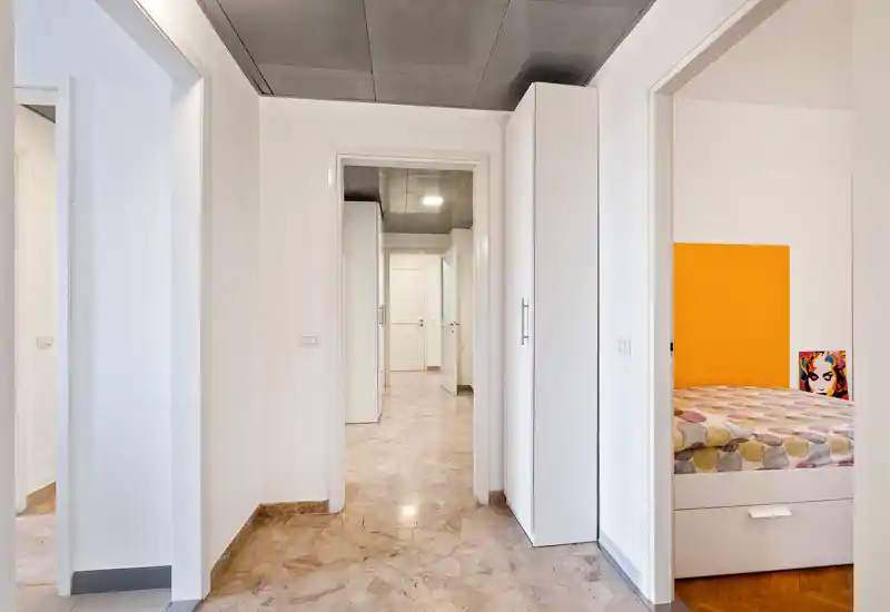Bright, clean hallway/entrance with marble flooring and white walls leading to multiple rooms; built-in storage cabinet on the right and a view into a bedroom on the right.