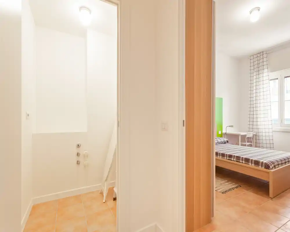 Dormitorio luminoso y sencillo con cama de madera, ropa de cama a cuadros y ventana que aporta luz natural. Dispone de un pequeño escritorio junto a la ventana y una decoración moderna y neutra.