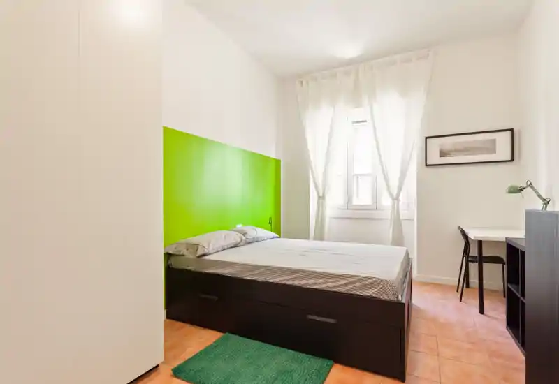 Dormitorio luminoso y moderno con cabecero verde, cama doble con cajones de almacenamiento, escritorio y luz natural desde la ventana: espacio limpio y acogedor ideal para descansar.