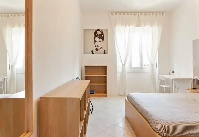 Camera da letto luminosa e minimale con letto matrimoniale, mobili in legno chiaro e tende leggere che illuminano l'ambiente con luce naturale.