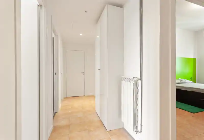Bright, clean entrance corridor with tiled floor and built-in storage, leading to other rooms. Neutral white walls provide a modern, minimal feel.