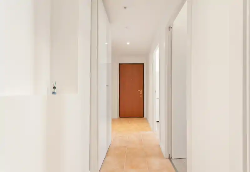 Bright, minimal entrance hallway with tiled floor and a wooden front door; clean white walls and recessed ceiling lights create a welcoming first impression.