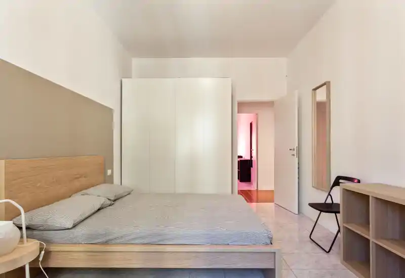 Dormitorio luminoso y minimalista con cama doble de madera, ropa de cama a rayas, armario blanco empotrado y estantería sencilla — líneas limpias y tonos neutros que transmiten calma.