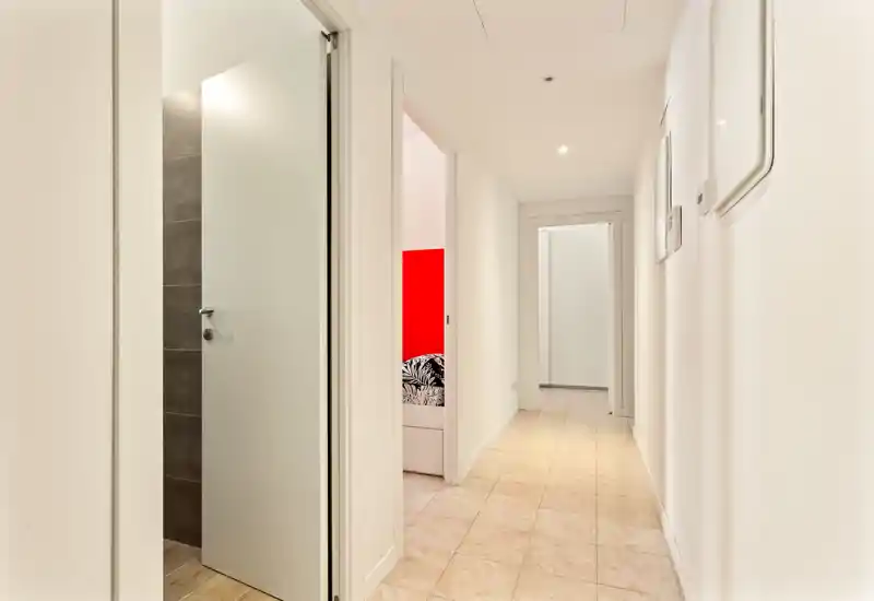 Bright, clean hallway with tiled floor and white walls leading to multiple rooms; well-lit entrance corridor ideal for apartment listings.