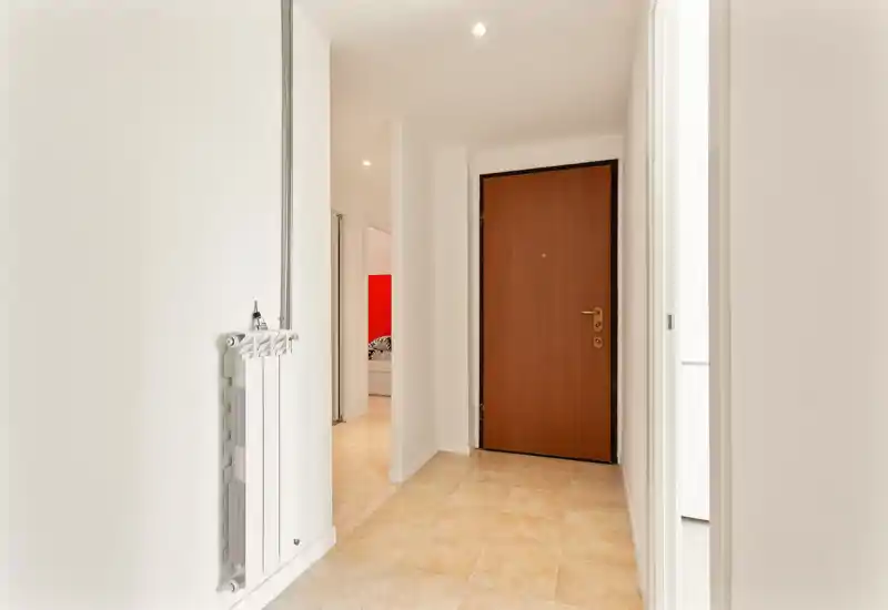 Clean, bright entrance hallway with tiled floor and a solid wooden front door; neutral white walls and recessed ceiling lights create a welcoming first impression.