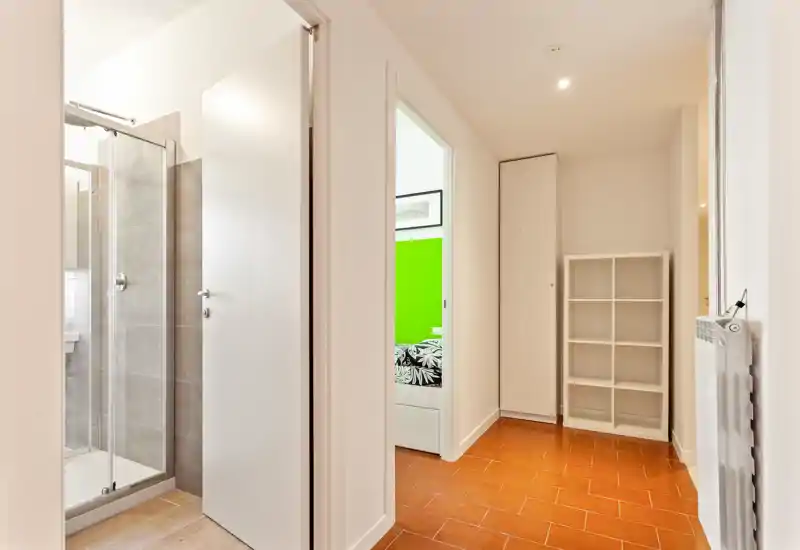 Bright, clean entrance corridor with terracotta floor tiles, built-in storage and a visible bathroom doorway; simple modern styling and good natural/artificial light.
