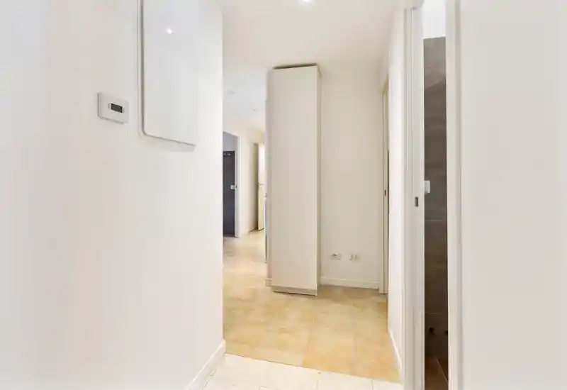 Bright, minimal entrance hallway with light tiled flooring and clean white walls; practical layout leading to adjacent rooms.