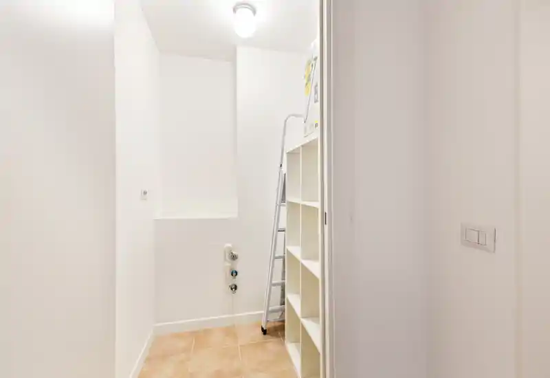 Small utility/entrance niche with tiled floor, white walls and shelving — suitable for laundry or storage.