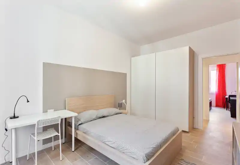 Dormitorio moderno y luminoso con cama doble, escritorio minimalista y gran armario; tonos neutros y líneas limpias, ideal para anuncios de alquiler.