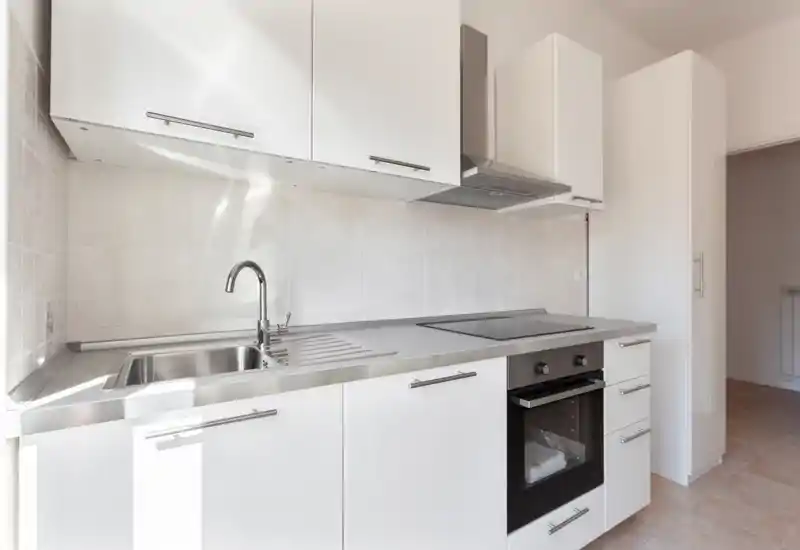 Cucina moderna e compatta con mobili bianchi, lavello in acciaio, piano a induzione e forno integrato; design luminoso e minimale perfetto per annunci.