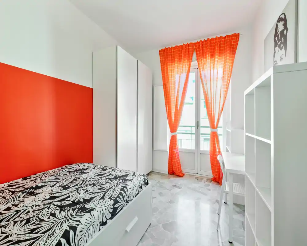 Dormitorio moderno y luminoso con cama individual estampada, armarios blancos y amplia ventana-balcon con cortinas naranja llamativas — ambiente fresco y ventilado, ideal para estudiantes o estancias cortas.