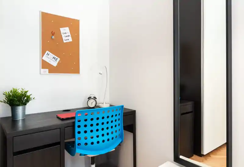 Acogedor rincón de trabajo luminoso con escritorio oscuro, silla azul perforada, tablero de corcho y pequeña planta decorativa — perfecto para concentrarse.