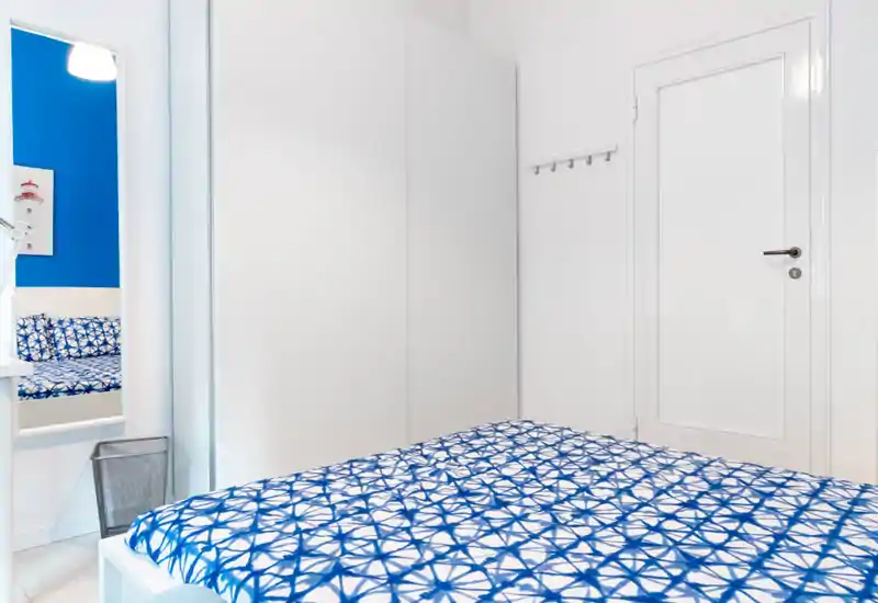 Dormitorio limpio y luminoso con armario blanco y colcha de motivos azules; estilo minimalista y alto contraste que aporta sensación de frescura y modernidad.