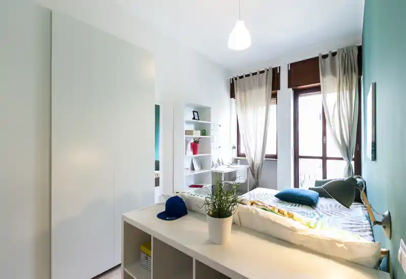 Bright, modern bedroom with a single bed near large windows, a built-in wardrobe and a tidy desk area — ideal for a single occupant or student.