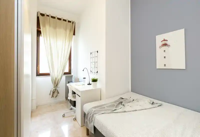 Bright, minimalist bedroom with a single bed, a compact desk by the window, and soft neutral tones — ideal for a student or single occupant.