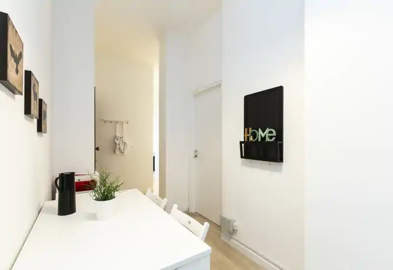 Angolo pranzo compatto e luminoso con tavolo bianco, sedie essenziali e decorazioni minimal alle pareti — ideale per colazioni o pasti veloci.