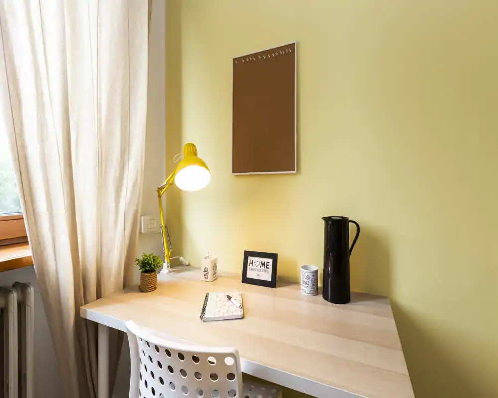 Coin bureau lumineux et soigné avec bureau en bois, lampe jaune et petite plante près de la fenêtre — parfait pour le télétravail ou les études.
