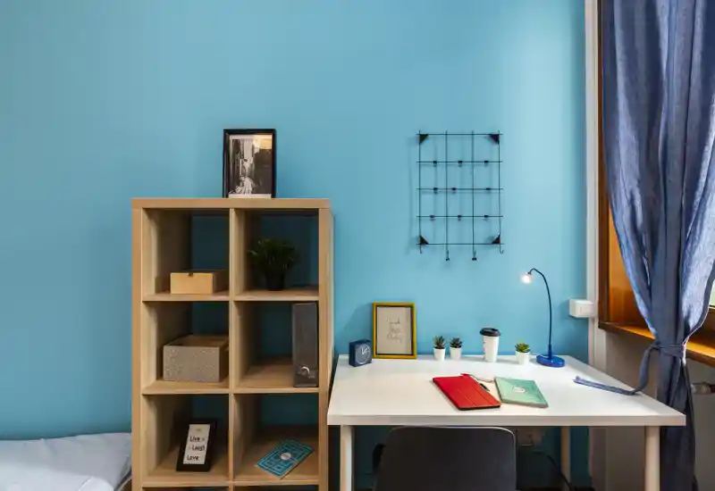 Camera da letto luminosa con parete turchese, mobile a cubi e una scrivania ordinata vicino alla finestra.