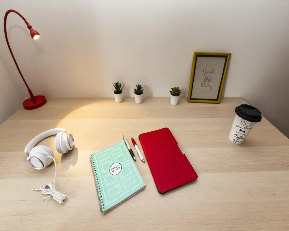 Rincón de escritorio luminoso y bien decorado con lámpara roja, suculentas, auriculares, libreta y tablet: un espacio de trabajo ordenado ideal para teletrabajo o estudio.