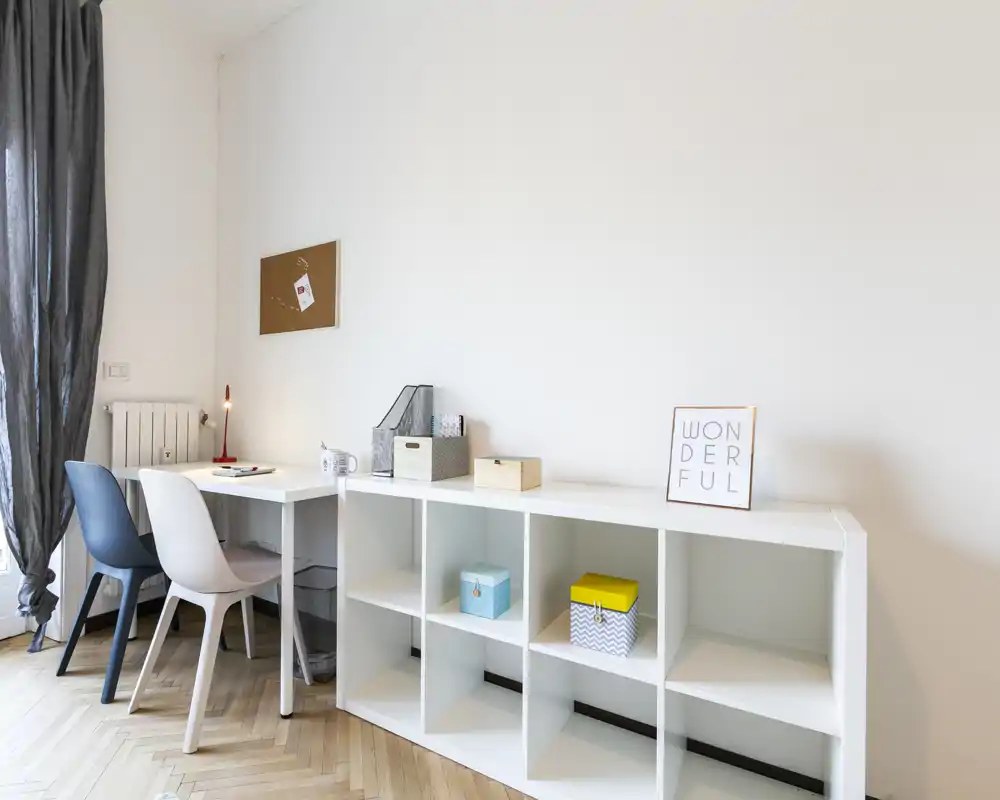 Angolo moderno e minimale living/studio con mobile contenitore bianco, scrivania e due sedie; luminoso, ordinato e adatto come piccolo ufficio domestico o area relax.