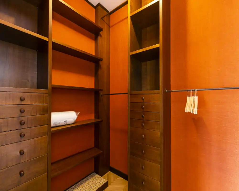 Cabina armadio / zona guardaroba con scaffalature in legno, cassetti e bastoni appendiabiti su pareti arancioni. Perfetta per riporre abiti e accessori in ordine.