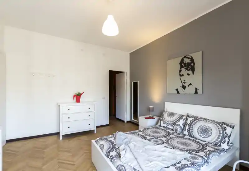Camera da letto moderna e luminosa con biancheria a motivi, struttura del letto bianca e comodino; un semplice cassettone e un quadro rendono l'ambiente accogliente e pulito.