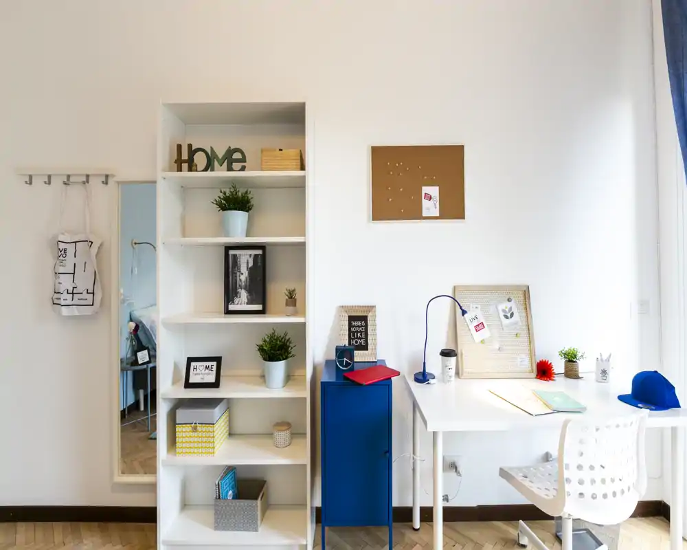 Rincón luminoso y moderno de trabajo/estar con estanterías blancas, un escritorio pequeño y accesorios decorativos que crean un ambiente acogedor.