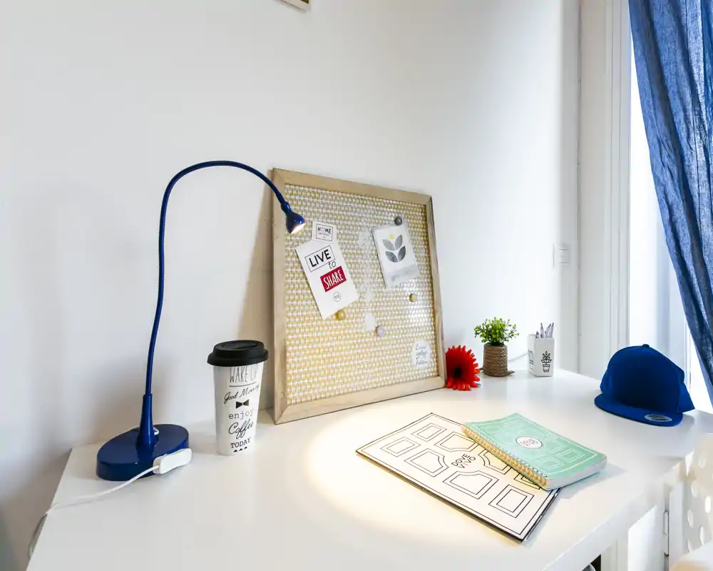 Rincón de escritorio luminoso y ordenado con lámpara, corcho, cuaderno y planta pequeña, ideal para trabajar.