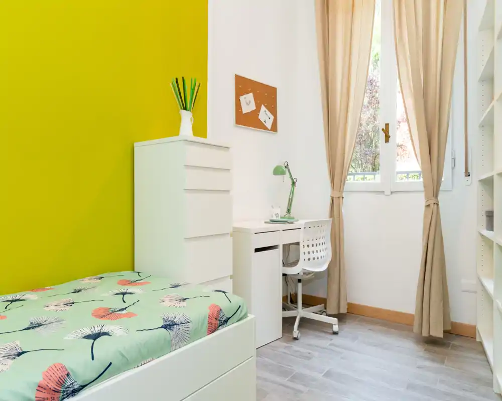 Sunny, modern single bedroom with a patterned bed, white storage drawers and a small study desk by the window — bright, tidy and ideal for a student or single occupant.