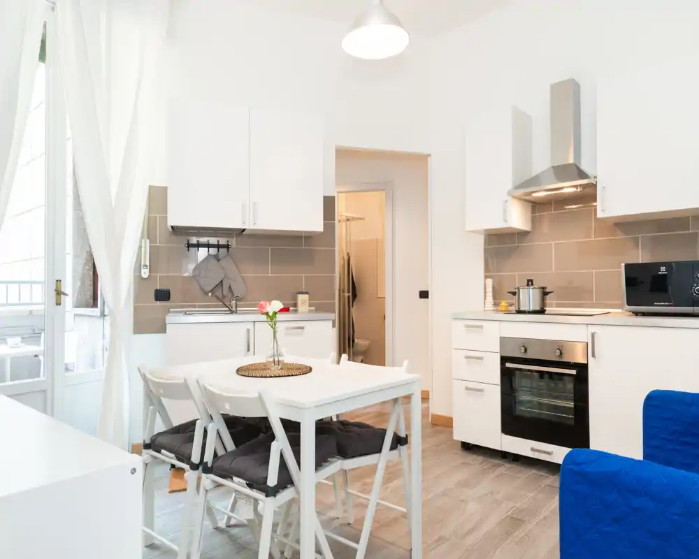 Bright modern kitchen with white cabinets, built-in oven and a small dining table; natural light and simple, welcoming décor.