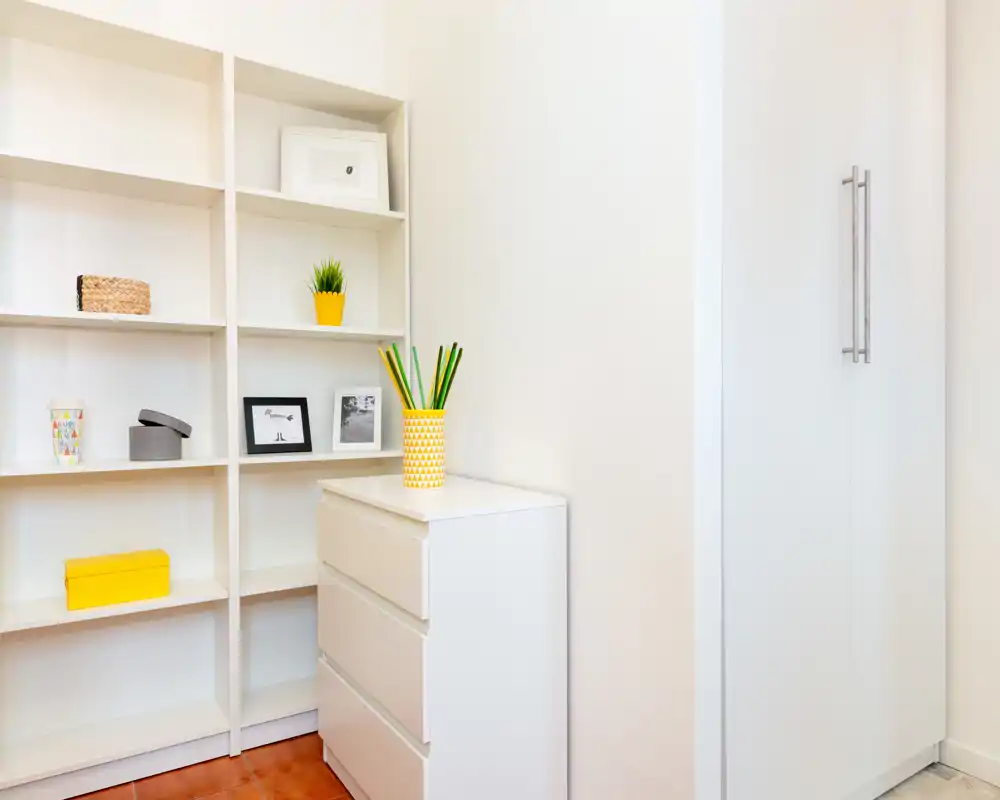 Bright, minimal entrance or small hallway corner with built-in shelving and a white chest of drawers; decorative accents in yellow add a fresh, organized look.