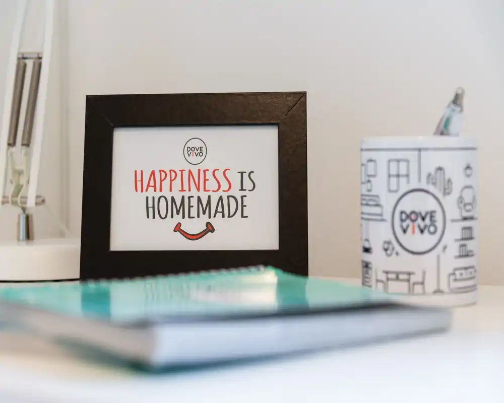 Close-up of a decorative framed sign on a desk with stationery and a lamp; a styled detail shot rather than a full room view.