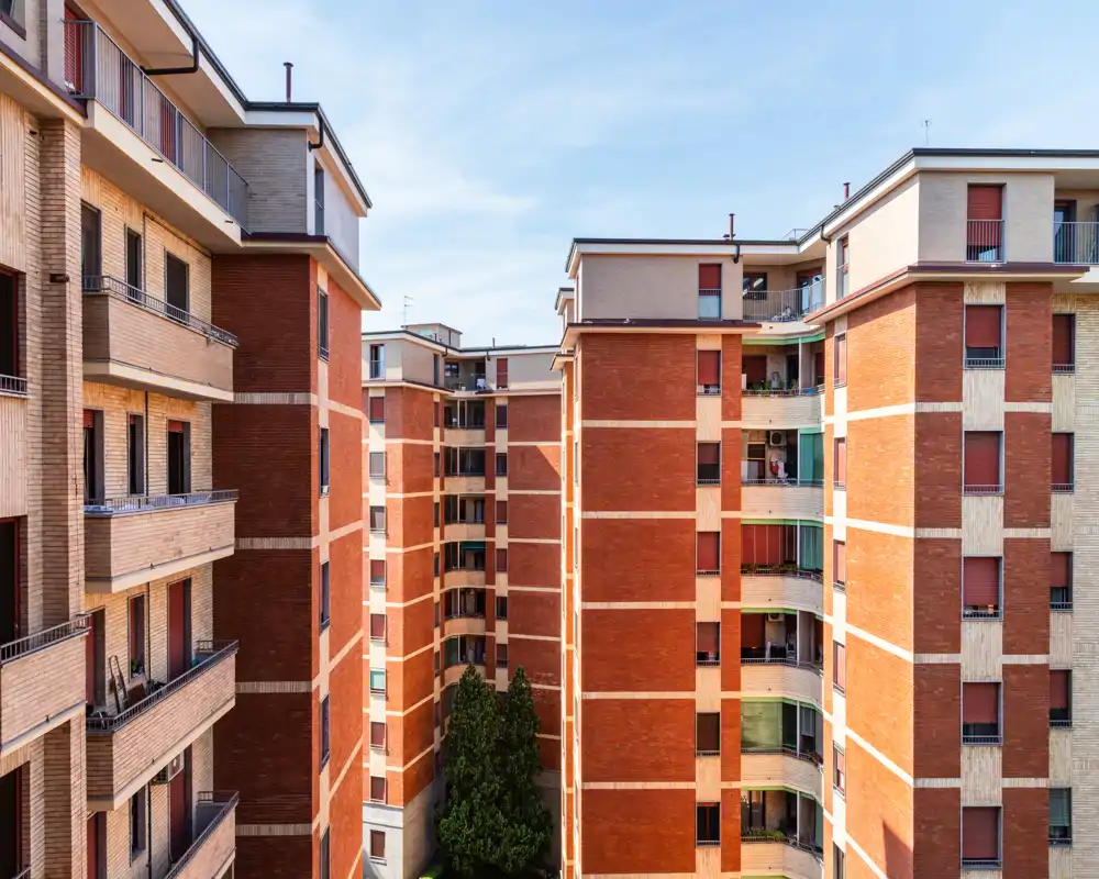 Vista exterior de un patio residencial enmarcado por edificios de apartamentos de ladrillo de varios pisos con balcones y persianas, tomada en un día despejado.