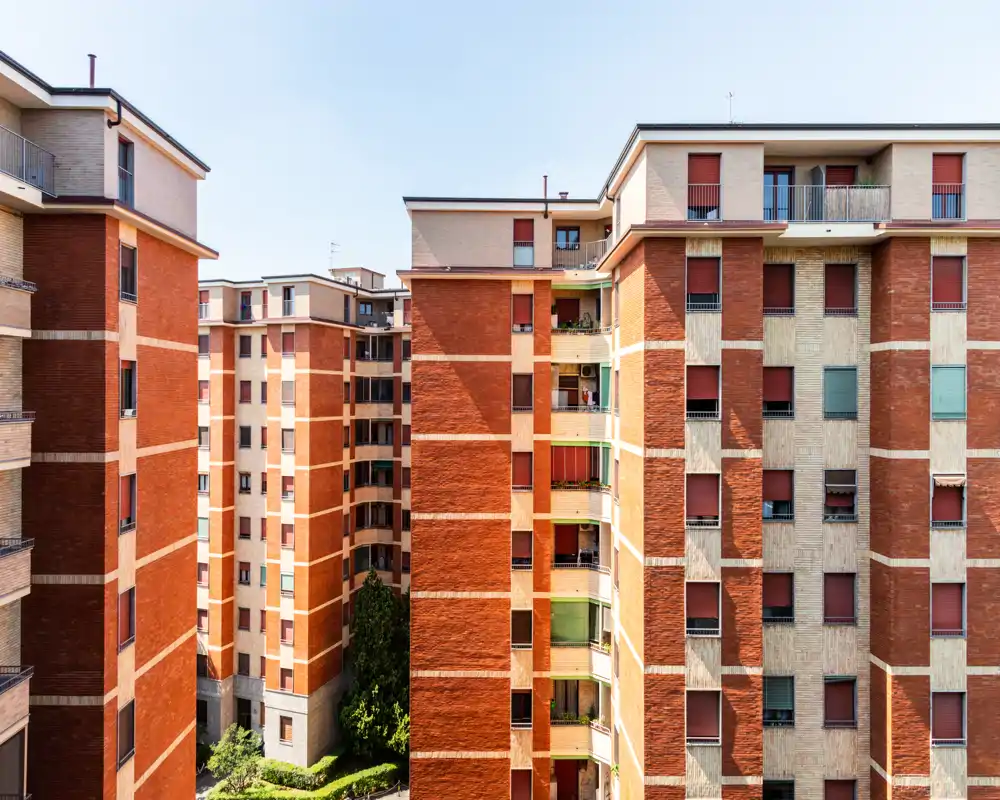 Vista exterior de bloques de apartamentos residenciales con fachadas de ladrillo rojo y balcones, tomada en un día claro y soleado.