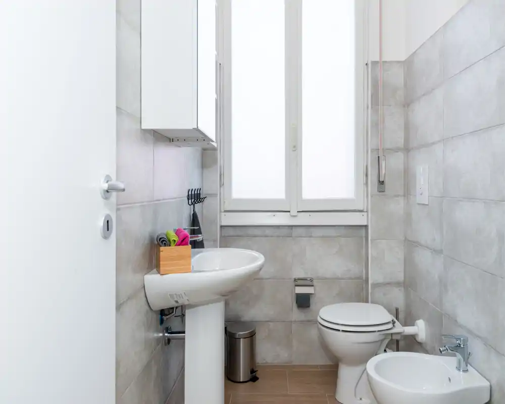 Baño moderno y luminoso con lavabo de pedestal, inodoro y bidé en un espacio alicatado de tonos neutros — limpio y de estilo sencillo para anuncios.