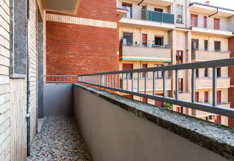 Balcony view with tiled floor, concrete parapet and metal railing overlooking neighboring brick apartment facades — bright, practical outdoor space.