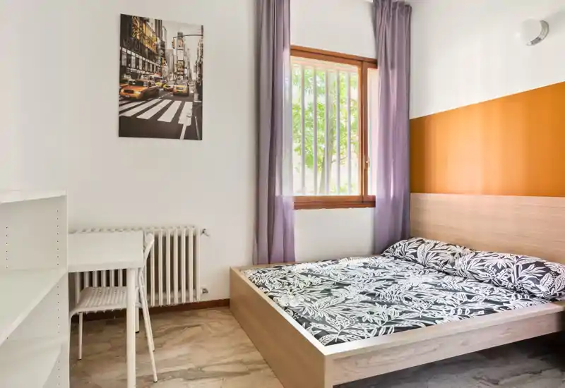 Bright, tidy bedroom with a double bed featuring patterned bedding, a wooden headboard and natural light from the window — ideal for short-term rentals.