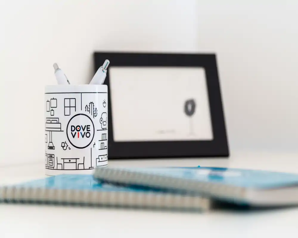 Primer plano de un rincón de escritorio con un portalápices con marca, cuadernos en espiral y un marco de fotos desenfocado: toma de detalle minimalista del espacio de trabajo.